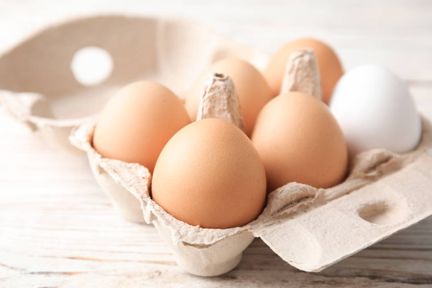 Carton of raw chicken eggs on wooden background, closeup - Fotó, kép