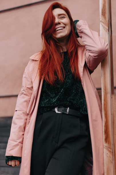 Beautiful and stylish girl with red hair walks in the city and her hair is in the wind - Valokuva, kuva