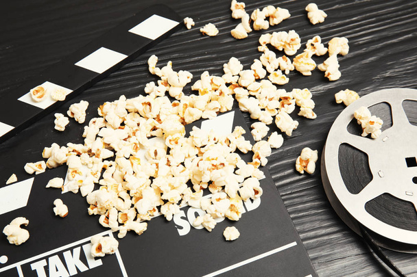 Tasty popcorn, film reel and clapperboard on wooden table. Cinema snack - 写真・画像