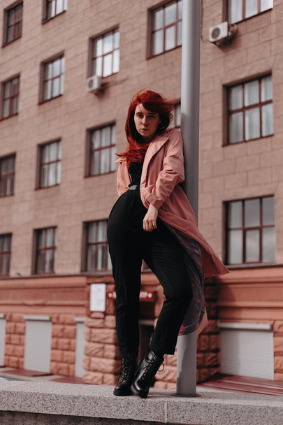 Beautiful and stylish girl with red hair walks in the city and her hair is in the wind - Фото, изображение