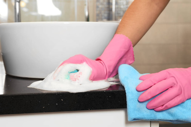 Frau in Schutzhandschuhen putzt Badezimmerarbeitsplatte mit Schwamm, Nahaufnahme - Foto, Bild