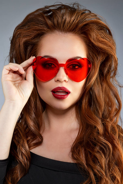 Cute girl with glasses in the shape of a heart. Funny, positive, funny model in red sunglasses. - Photo, image