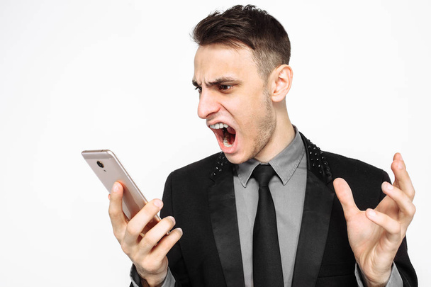 Деловой человек, в черном костюме, кричит от злости в смартфоне, на белом фоне
, - Фото, изображение