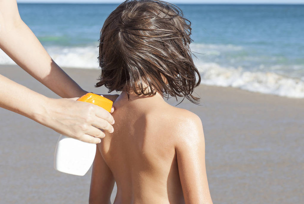 Moeder sunblock cream met spuitpistool toe te passen op haar dochter achterop. Idyllisch beach achtergrond  - Foto, afbeelding