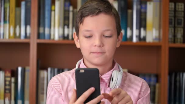portret strzał Ładna uczniak z smartphone stojący w pobliżu na półce w bibliotece - Materiał filmowy, wideo