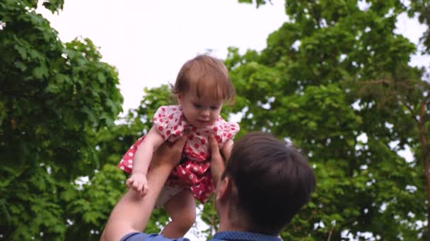 Papá juega con un niño en el verano en el parque. La niña está saltando en el aire en manos de papá y riendo. Movimiento lento
 - Metraje, vídeo