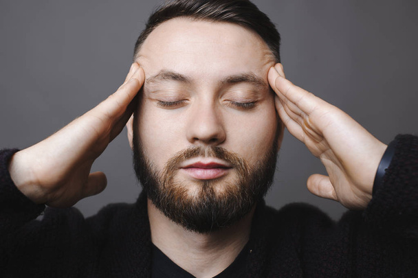Hezký vousatý muž udržet oči zavřené při stání na šedém pozadí a myšlení - Fotografie, Obrázek