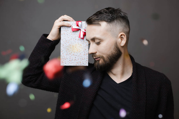 Colorful confetti falling down in front of attractive male with gift box on gray background - Valokuva, kuva
