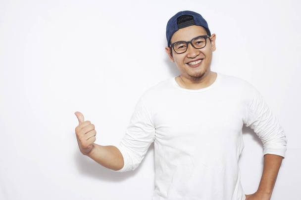 Young Asian man wearing white shirt smiling, showing and pointing something on his side, against white wall with copy space. Close up body portrait - Фото, зображення