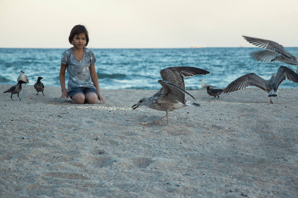 όμορφο κοριτσάκι που παίζουν στην αμμώδη παραλία με γλάρους σε ηλιόλουστη ημέρα  - Φωτογραφία, εικόνα