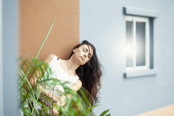 attractive woman with closed eyes leaning on building wall  - Фото, изображение