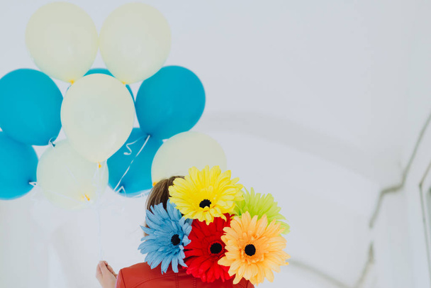 A woman holding balloons and paper flowers. Holiday concept, red jacket, bright colours. Red, yellow, blue. - Photo, Image