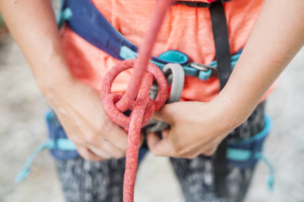 Ein Bergsteiger knüpft einen Knoten. Eine Frau bereitet sich darauf vor, eine Kletterroute zu erklimmen. Versicherung und Sicherheit beim Klettern. Sicherheitsseil. Knoten acht. - Foto, Bild