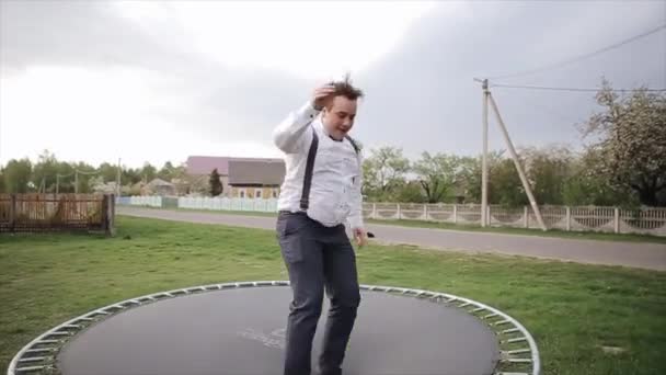 Hyvin pukeutunut mies pomppii ja pitää hauskaa trampoliinilla ulkona
 - Materiaali, video