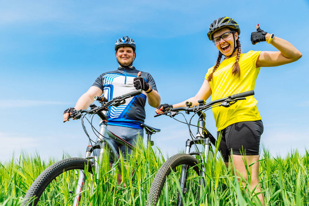 joven sonriente hombre fuerte y mujer de pie en el campo verde con bicicletas. estilo de vida
 - Foto, imagen