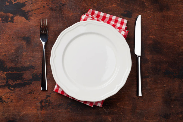Empty plate, knife, fork and napkin on wooden background  - Фото, изображение
