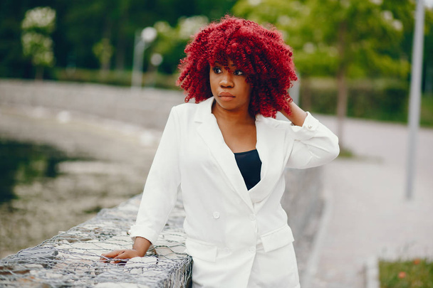 Stylish black girl in a park.  Fashionable woman in a summer city. Curly lady in a white jacket. - Foto, Imagen