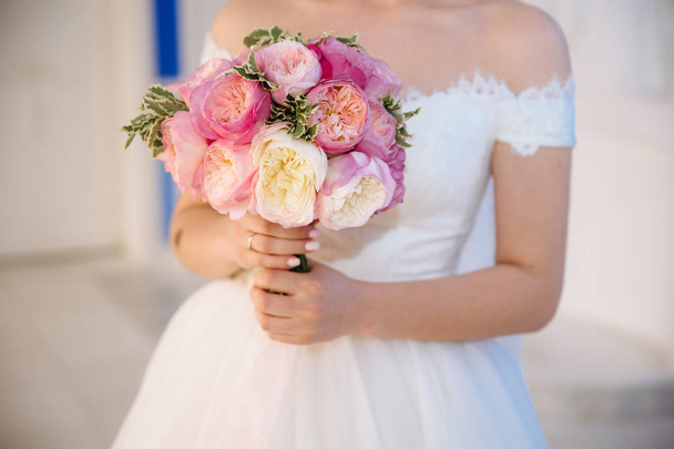 A close-up of a cropped wedding frame is a tender bouquet of roses in the hands of the bride. A girl in a wedding dress is holding flowers. - Valokuva, kuva