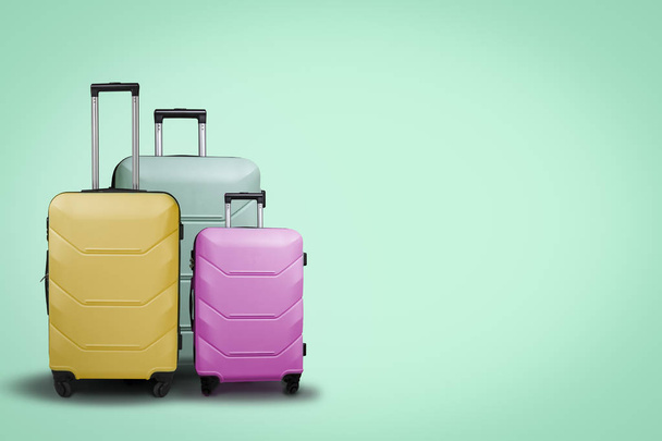 Three multi-colored plastic suitcases on wheels on a green background. Travel concept, vacation trip, visit to relatives. - Фото, зображення