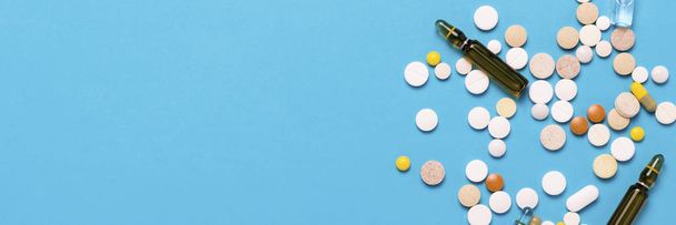 Pills of different colors and ampoules with medicine on a blue background. Concept of the pharmaceutical industry, medicine, treatment and recovery after illness. Banner. Flat lay, top view. - Foto, Bild