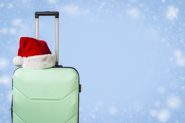 Plastic suitcase, Santa Claus hat on blue background with snow. Concept of travel to visit friends and relatives on Christmas holidays. Merry Christmas and Happy New Year. Christmas trip. - Fotografia, imagem