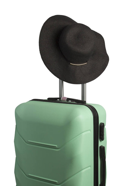 Plastic suitcase on wheels and a hat with a wide brim on the handle on a white background. Isolated. Travel concept, vacation trip, visit to relatives. - Foto, Bild