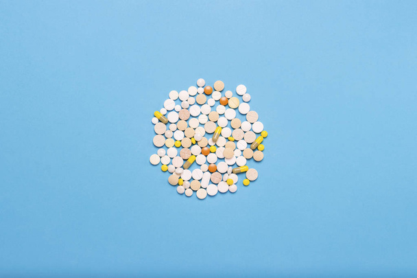 Pillen in verschillende kleuren en maten op een blauwe achtergrond. de vorm van de cirkel. Concept van de farmaceutische industrie, de geneeskunde, de behandeling en het herstel na ziekte. Plat lag, top uitzicht. - Foto, afbeelding