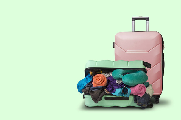 Opened plastic suitcase with wheels, crowded with things and a smaller suitcase standing next to a green background. Travel concept, vacation trip, visit to relatives. - Foto, Imagem