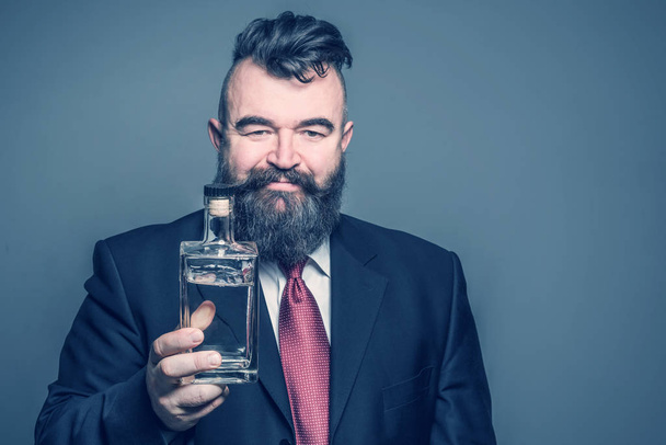 Adult bearded man in suit holding a bottle of alcohol - Фото, зображення