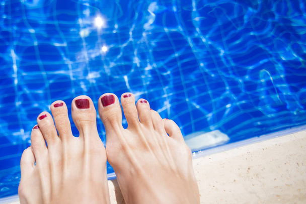 Female feet with red nail polish near the edge of the pool - Fotó, kép