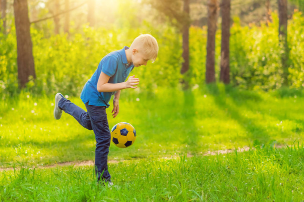 Blond boy in a blue T-shirt playing with a ball outdoors - Fotó, kép