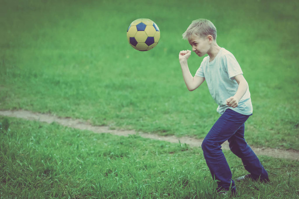 Blond boy in white t-shirt playing with soccer ball on green grass. Toned - Foto, Imagen