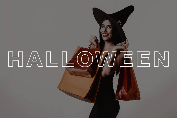 Halloween. Studio. Sexy. Half-Turn. Young Woman. Sale. Black Dress. Witch Hat. Packages. Magic. Fun. Fashion. Pretty. Lady. Glamour. Makeup. Wizard. Stylish. Shop Space. Gothic. Cosmetic. - Photo, image