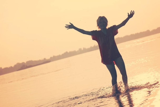 Dospívající dívka stojící ve vodě s zvednuté ruce při západu slunce - Fotografie, Obrázek