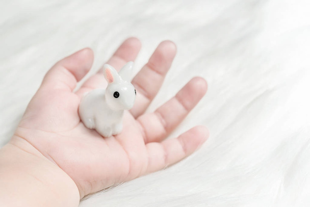 Figurine of a white rabbit in a baby's hand - Foto, afbeelding