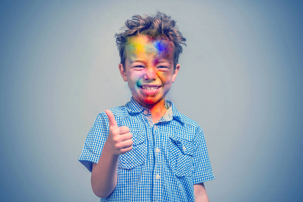 Smiling boy with a multicolored face in blue shirt showing thumb up - Foto, Bild