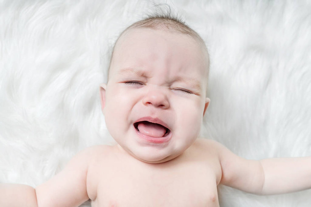 Crying baby lies on a white fluffy background - Zdjęcie, obraz