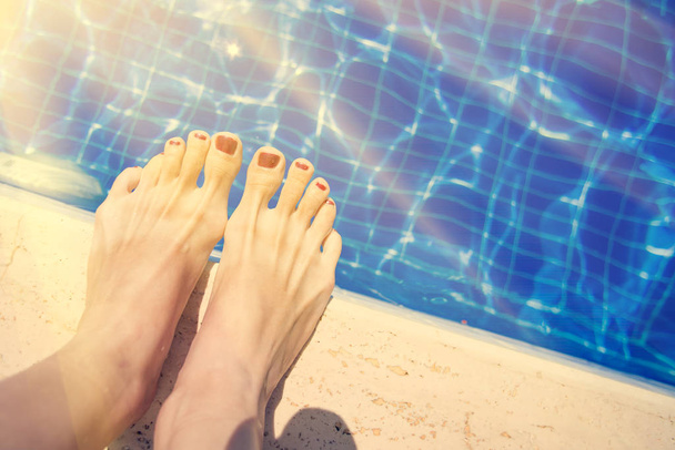 Female feet with red nail polish near the edge of the pool - Foto, Imagen