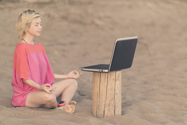 Girl with a red blouse meditating in front of laptop on the beach - Photo, image