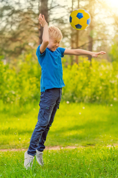 Blond garçon dans un T-shirt bleu lancer la balle dans le parc
 - Photo, image