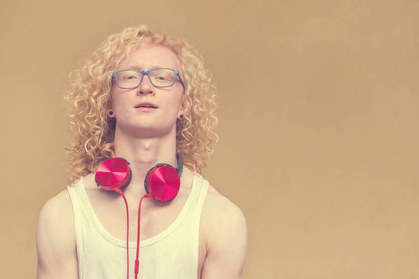 Curly blond man with glasses, red headphones around his neck and a white shirt on a yellow background - Foto, Imagen