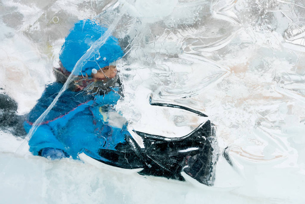 Little boy sitting on a sled behind a transparent ice - Fotó, kép