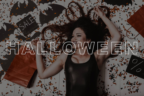 Halloween. Sexy Vampire. Dark Hair. Surrounded Confetti. Paper Bats. Bag. Sale. Young Woman. Black Dress. Sexy. Magic. Fun. Fashion. Pretty. Lady. Glamour. Makeup. Wizard. Stylish. Gothic. Cosmetic. - Foto, afbeelding