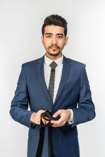 Young attractive man in a blue suit holding tie in hand on a white background. Isolated - Valokuva, kuva