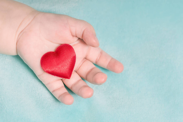 Red heart in the hand of a baby on a blue background - Фото, зображення
