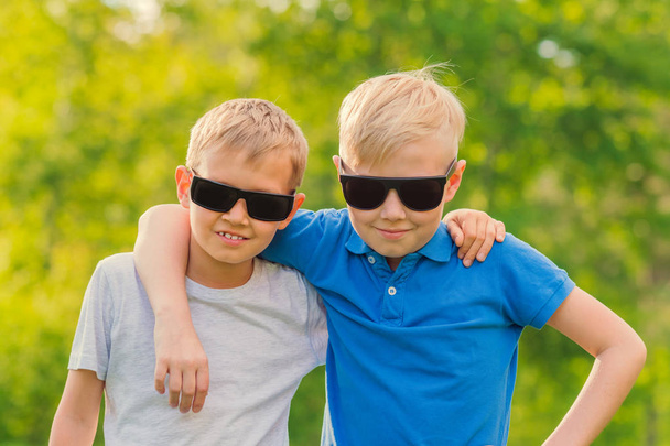 Two blonde boys in sunglasses standing hugging in the park - Zdjęcie, obraz