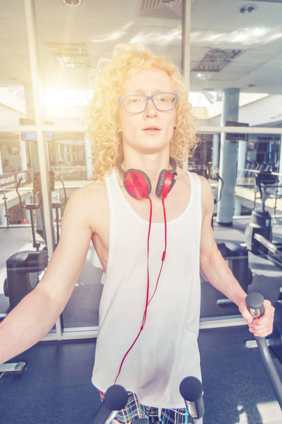 Curly blond man in glasses is trained in the gym in the sunlight - Photo, Image