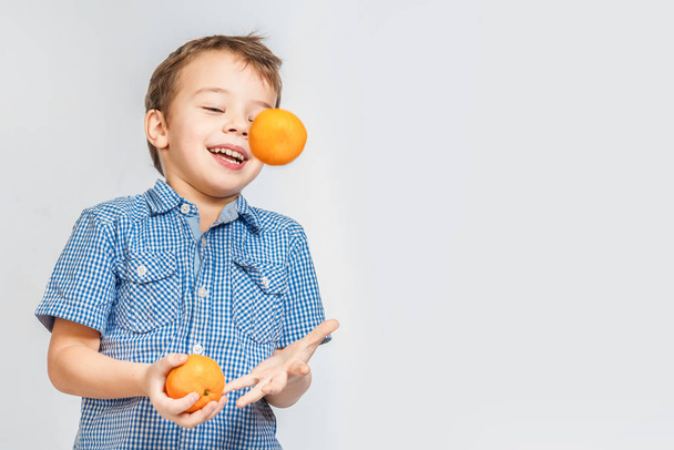 Cute smiling boy juggles with mandarins on a white background. Isolated - Fotoğraf, Görsel