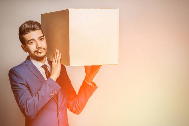 Attractive young man in a blue suit holding a cardboard box on his shoulder - Foto, Imagem