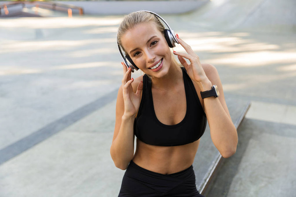 Obraz kobiety szczęśliwy młody fitness w parku słuchania muzyki ze słuchawkami. - Zdjęcie, obraz